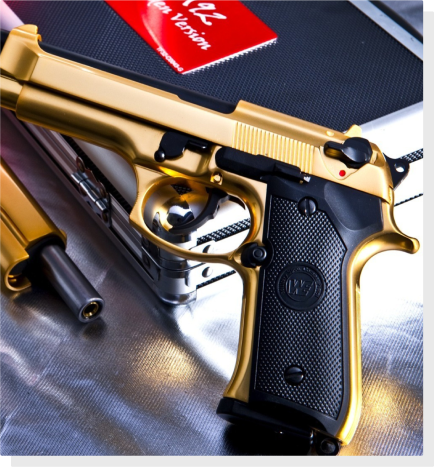 A gold color hand gun resting on a table with a hand gun case